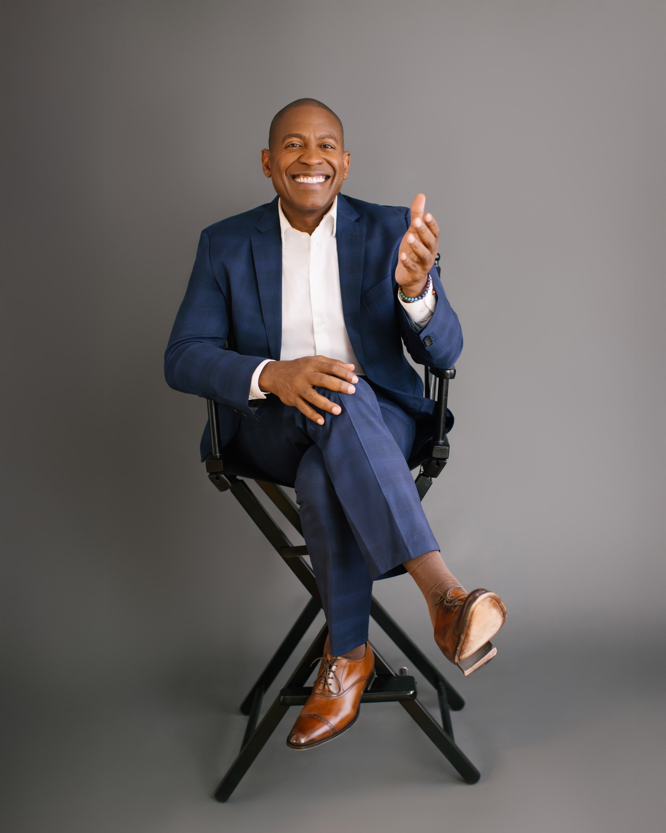 Carlos Watson seated in a director’s chair, mid-conversation