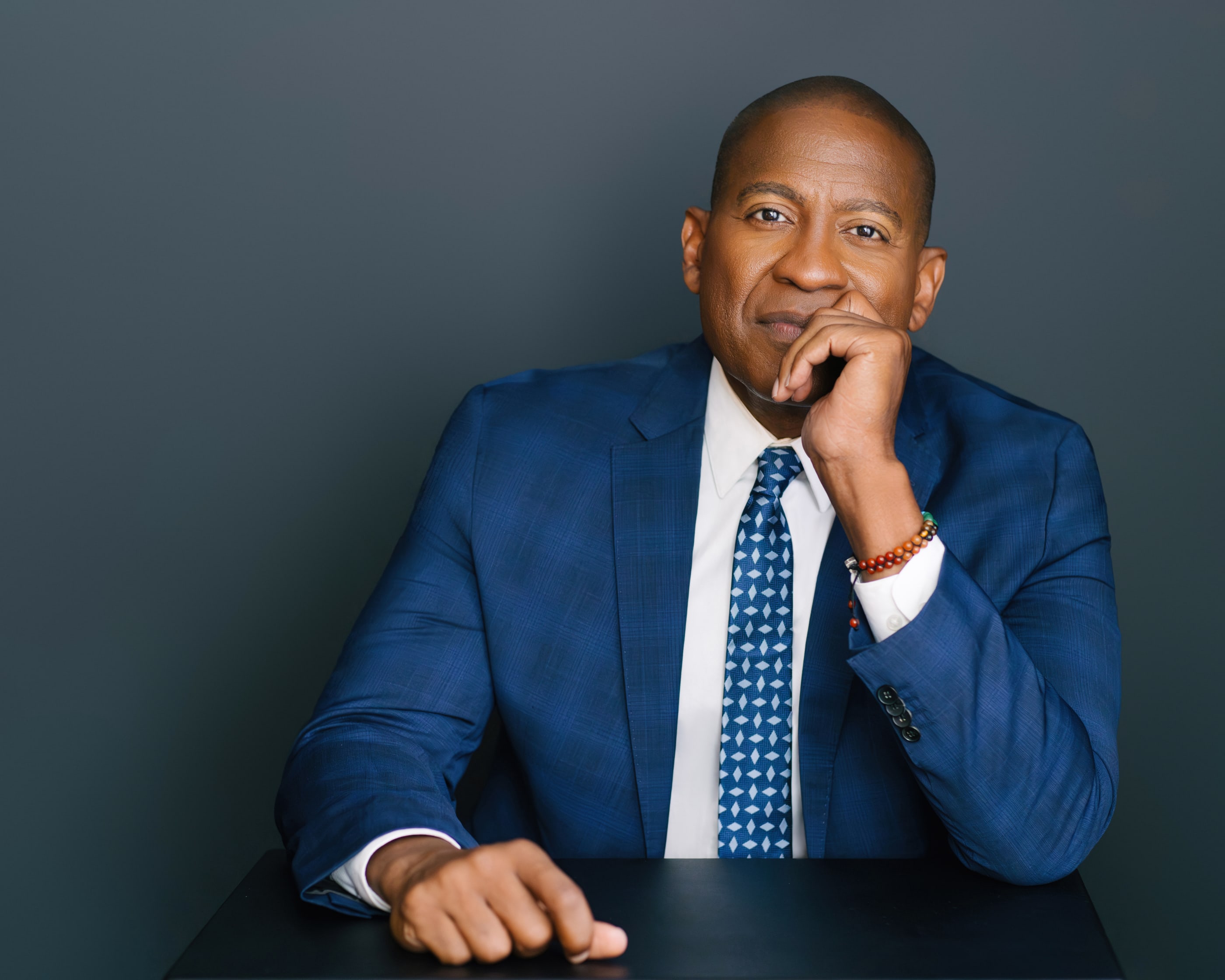 Carlos Watson seated at a desk, hand on chin